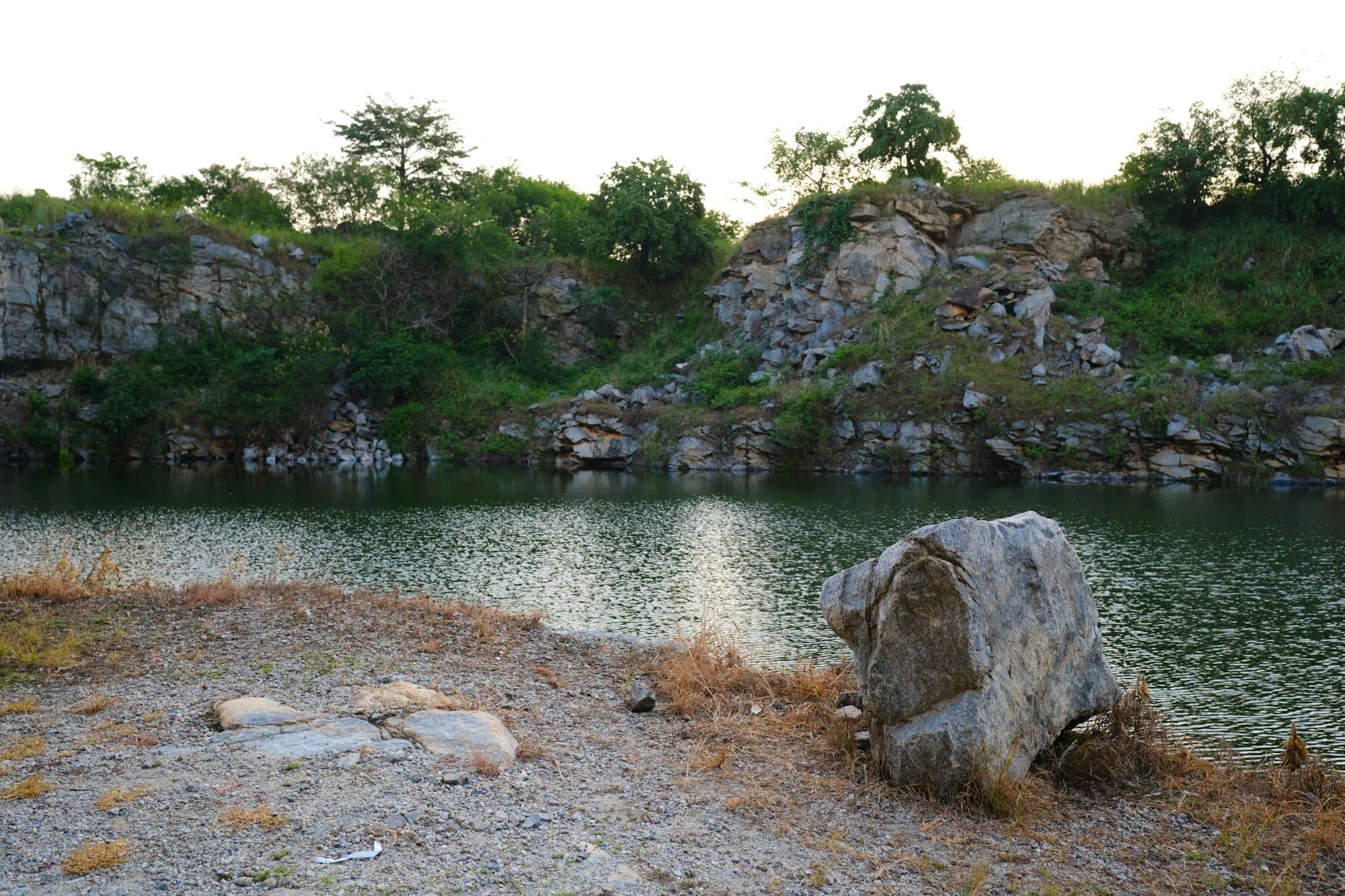 A still lake below rocky quarry walls and green vegetation
