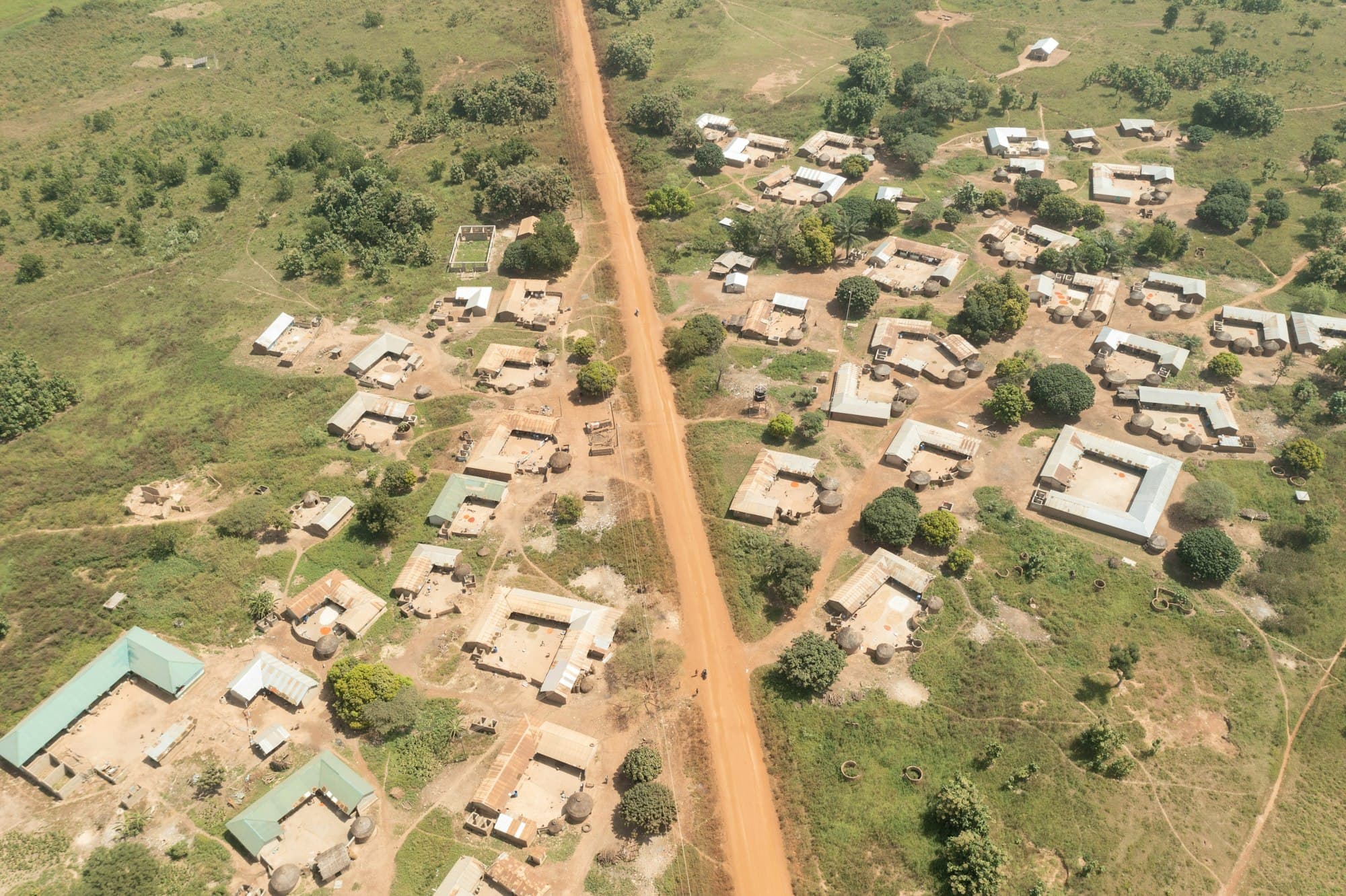 A village of compounds and a red earth road among fields, seen from above